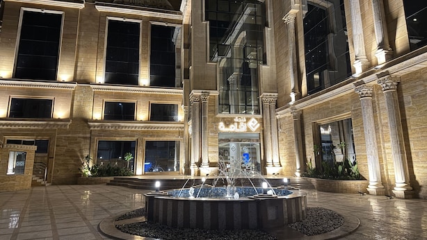 Um edifício imponente com uma fonte central, grandes janelas e elementos arquitetônicos clássicos.
