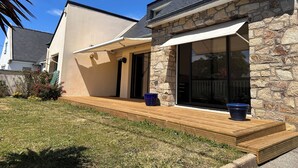Una casa con fachada de piedra, terraza de madera y zona de patio cubierta.