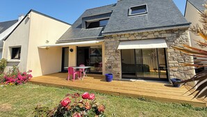 Una casa con fachada de piedra, una terraza de madera y un patio con mobiliario exterior.