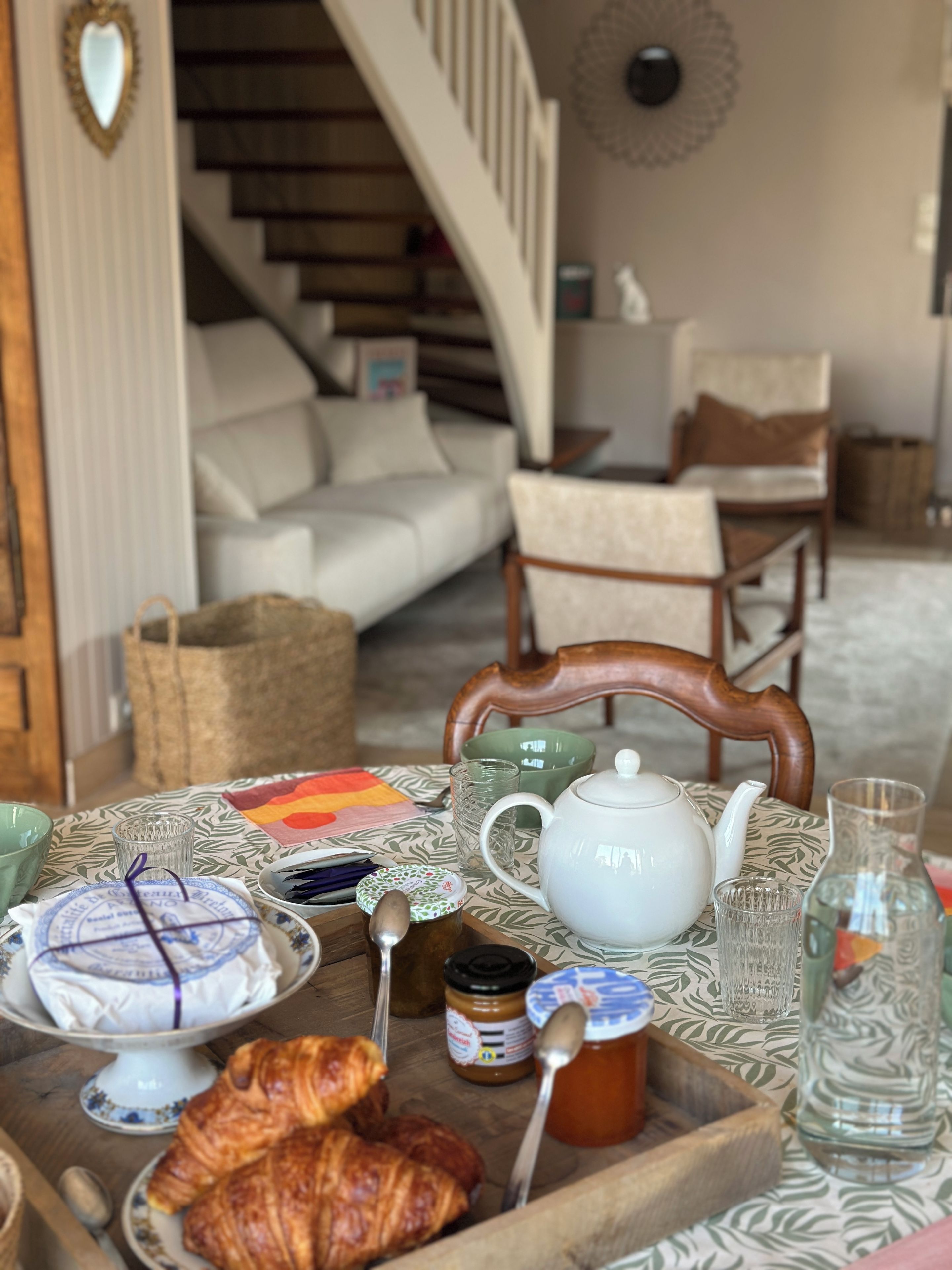 A breakfast setting with a table set for two, including a teapot, cups, a plate with pastries, and condiments.
