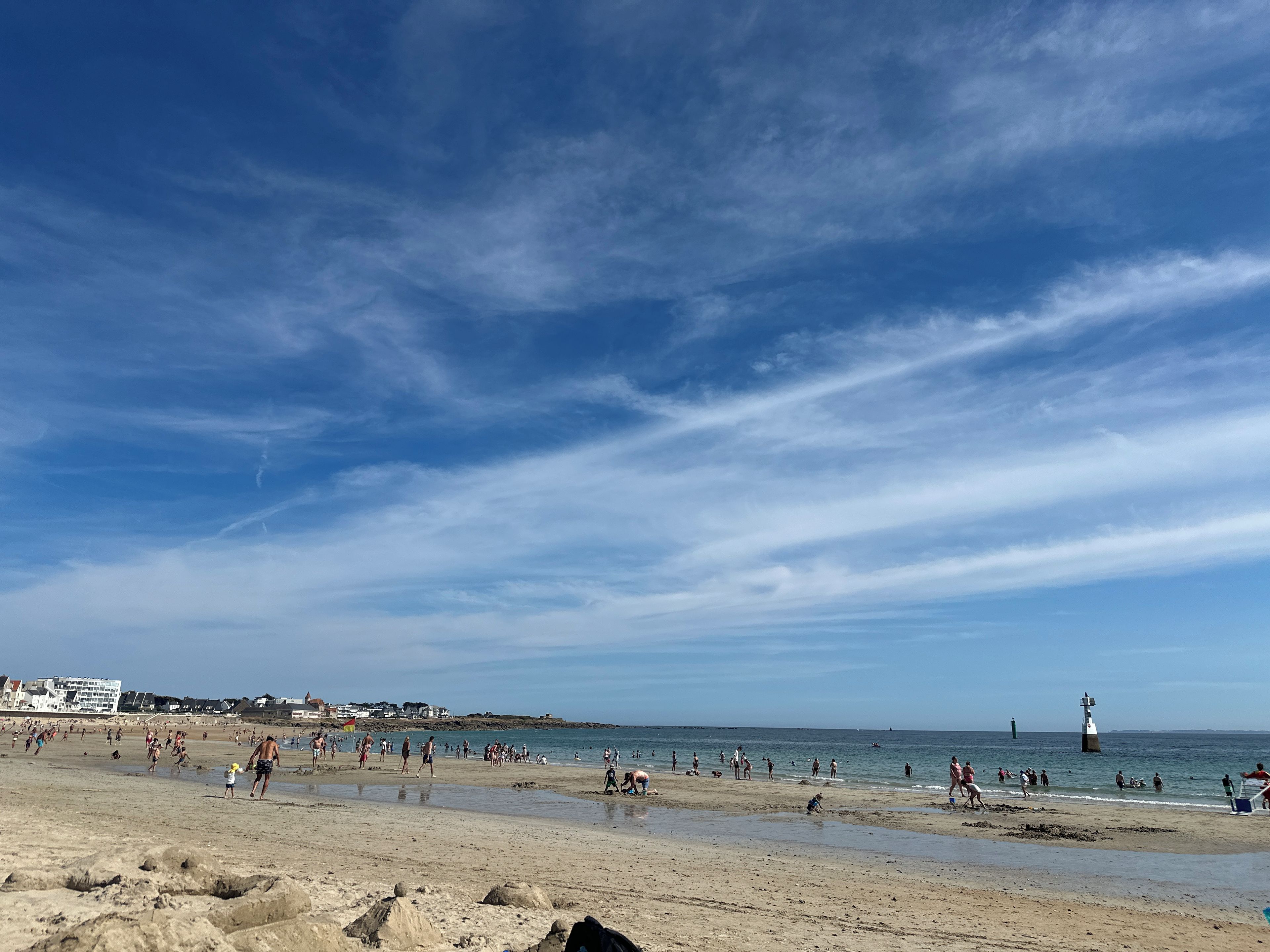 Una platja amb gent, un far i edificis al fons.