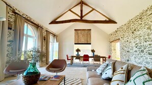 A spacious living area with a high ceiling, stone walls, and a dining area with red chairs. - 4-bedroom country house, sleeps 8, between Loire and Èvre (Mauges-sur-Loire)