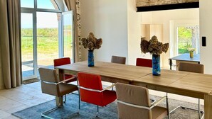 A modern dining room with a long table, red and beige chairs, and large windows. - 4-bedroom country house, sleeps 8, between Loire and Èvre (Mauges-sur-Loire)
