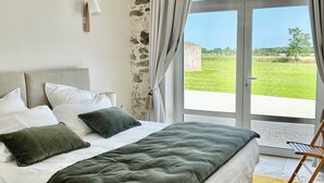 A bedroom with a bed, a nightstand, a lamp, and a view of the outdoors. - 4-bedroom country house, sleeps 8, between Loire and Èvre (Mauges-sur-Loire)
