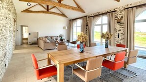 A spacious room with a high ceiling, exposed wooden beams, a large dining table, and modern furniture. - 4-bedroom country house, sleeps 8, between Loire and Èvre (Mauges-sur-Loire)
