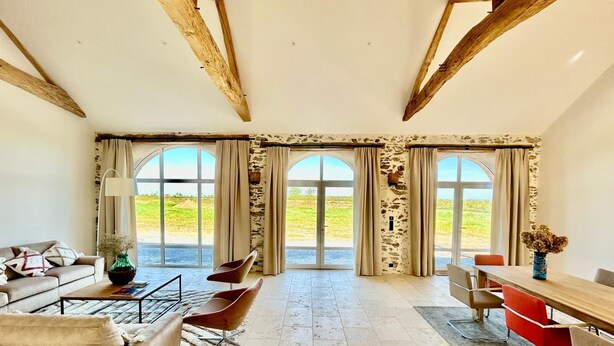 A spacious room with a large window, a sofa, a dining table, and a chair. - 4-bedroom country house, sleeps 8, between Loire and Èvre (Mauges-sur-Loire)