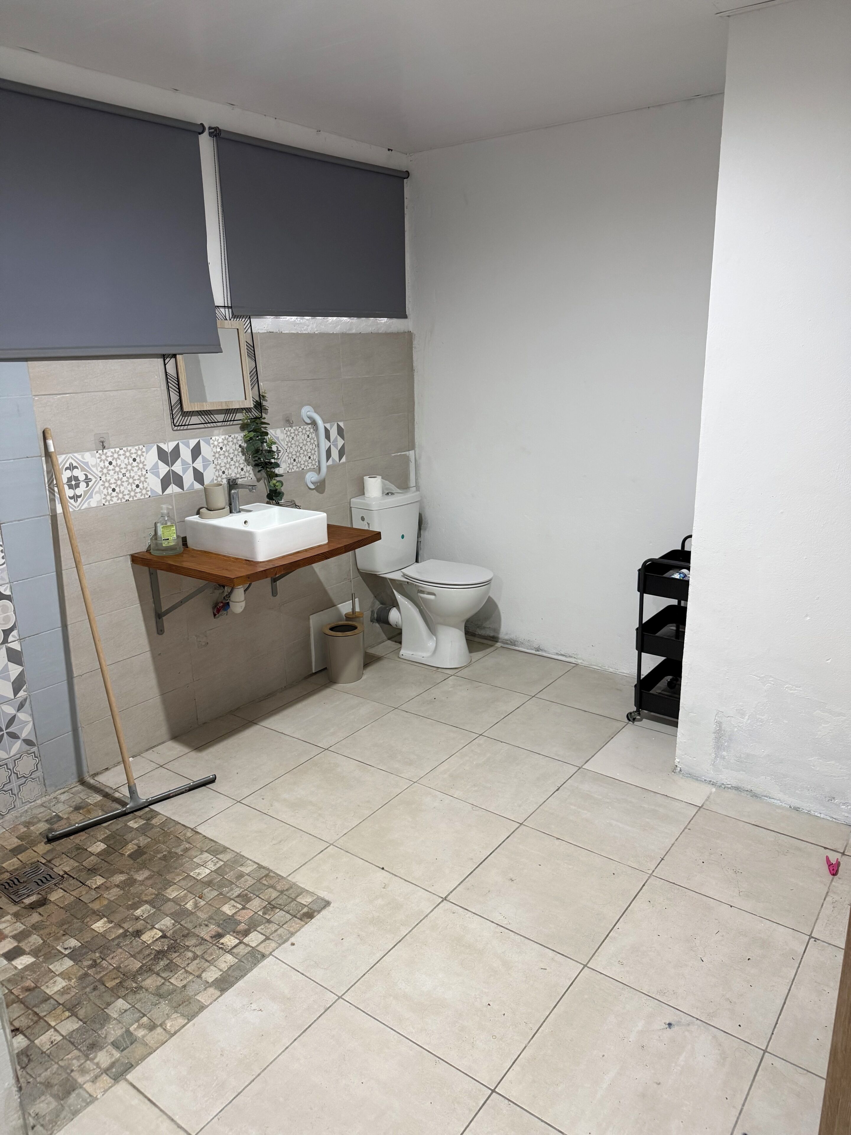 A bathroom with a toilet, sink, and a mop leaning against the wall.