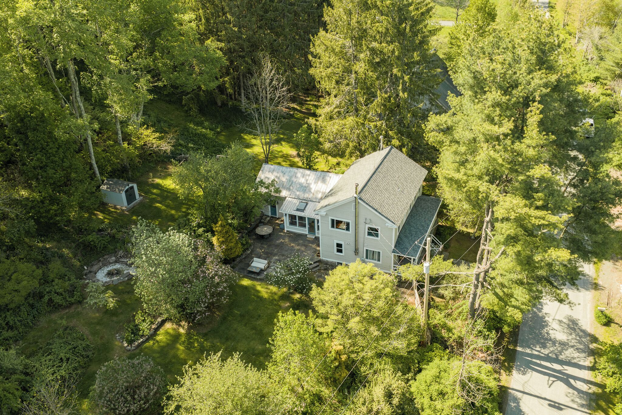 A house surrounded by dense forest, with a visible garage and a small pond.