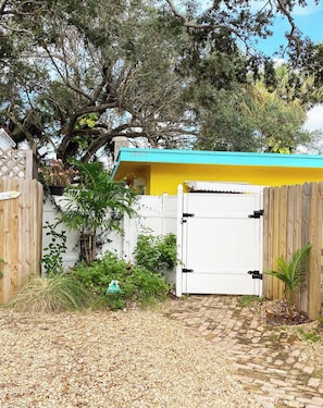 A gated entrance with a white door, a wooden fence, and a yellow building with a blue roof.