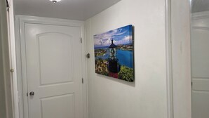 En hall med en vit dörr, en taklampa och en inramad tavla med ett motiv av en fyr på väggen.