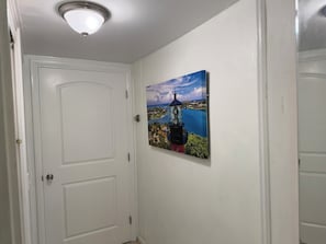 A hallway with a white door, a ceiling light, and a framed picture of a lighthouse on the wall.