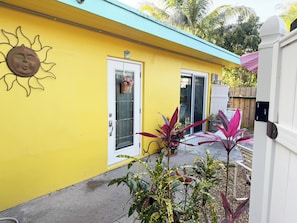 A yellow building with a sun-shaped decoration, a door with a window, and potted plants.