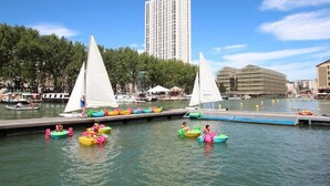 Une zone riveraine avec des voiliers, un quai et un grand immeuble en arrière-plan.