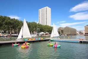 A waterfront area with sailboats, a dock, and a tall building in the background. - Les Frères Montgolfier - Les Canaux - 100m² - France (Paris)