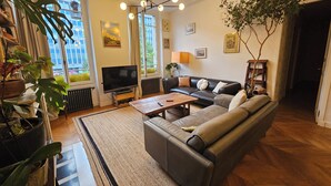 Un salon avec un canapé, une table basse, un téléviseur et de grandes fenêtres.