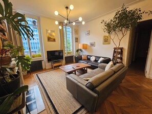A living room with a sofa, coffee table, TV, and large windows. - Les Frères Montgolfier - Les Canaux - 100m² - France (Paris)