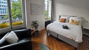 Une chambre à coucher avec un grand lit, un canapé en cuir noir, une plante en pot et une carte accrochée au mur.