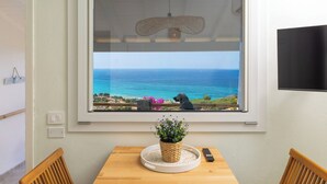 Ein Zimmer mit großem Fenster mit Meerblick, ein Holztisch mit Pflanze und Fernbedienung sowie ein an der Wand befestigter Fernseher.