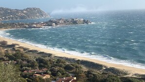 Blick auf die Küste mit Strand, Wellen und einem Felsen mit Gebäuden.