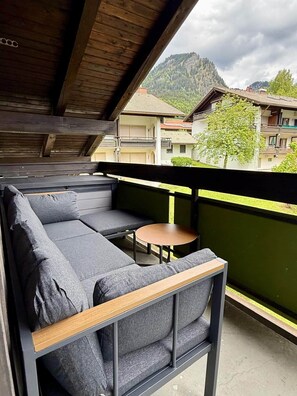 Ein Balkon mit einer Couch und einem kleinen Tisch, mit Blick auf eine gebirgige Gegend mit Gebäuden.