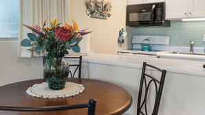 Zona pranzo con tavolo rotondo, sedie, un vaso con fiori, una cucina sullo sfondo e un'opera d'arte a parete.
