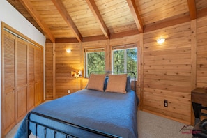 Ein Schlafzimmer einer Holzhütte mit einem Bett, zwei Fenstern, einem Kleiderschrank und einem Nachttisch.