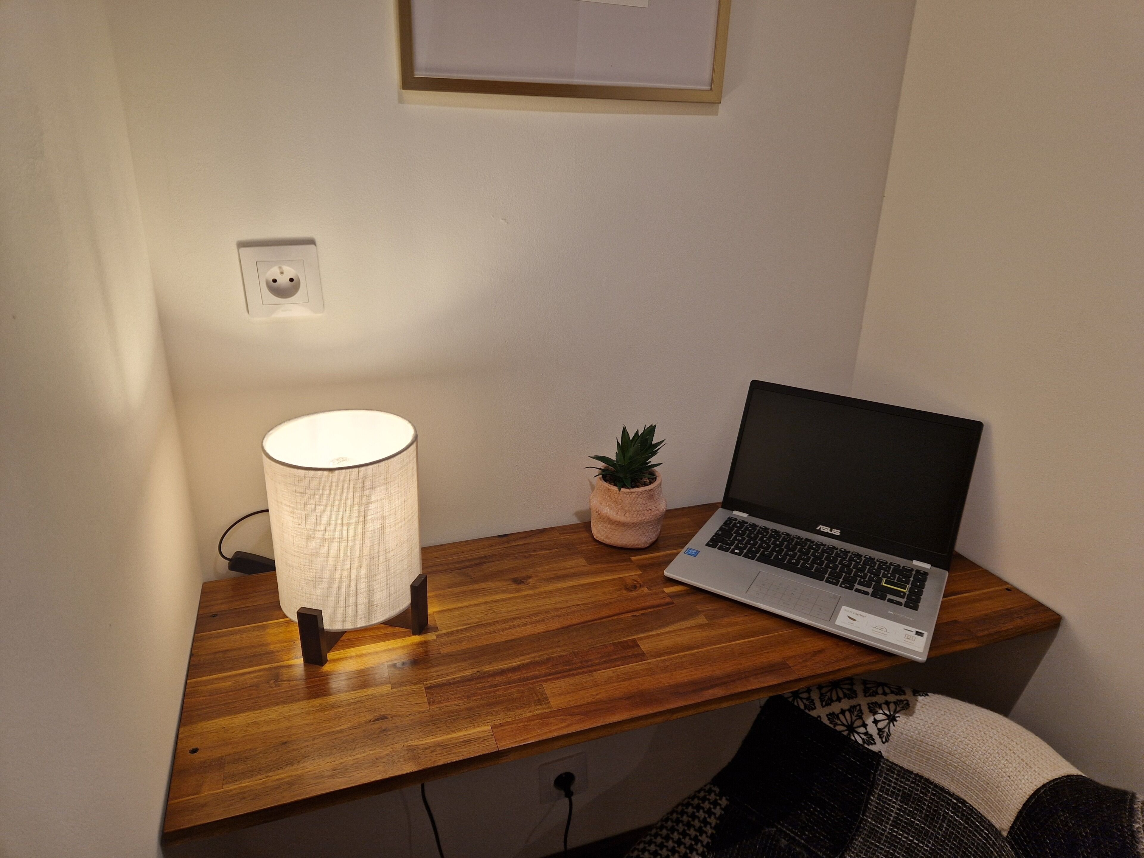 Ein Holztisch mit einem Laptop, einer Lampe und einem kleinen Topfpflanzen.
