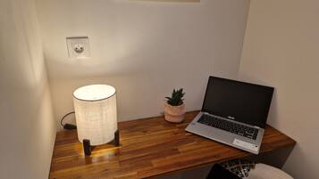 Ein Holztisch mit einem Laptop, einer Lampe und einem kleinen Topfpflanzen.