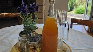 A table with a bottle of amber liquid, a glass pitcher, and small jars with lids, set on a wooden tray. - La Maison Argonnaise (Beaulieu en argonne)