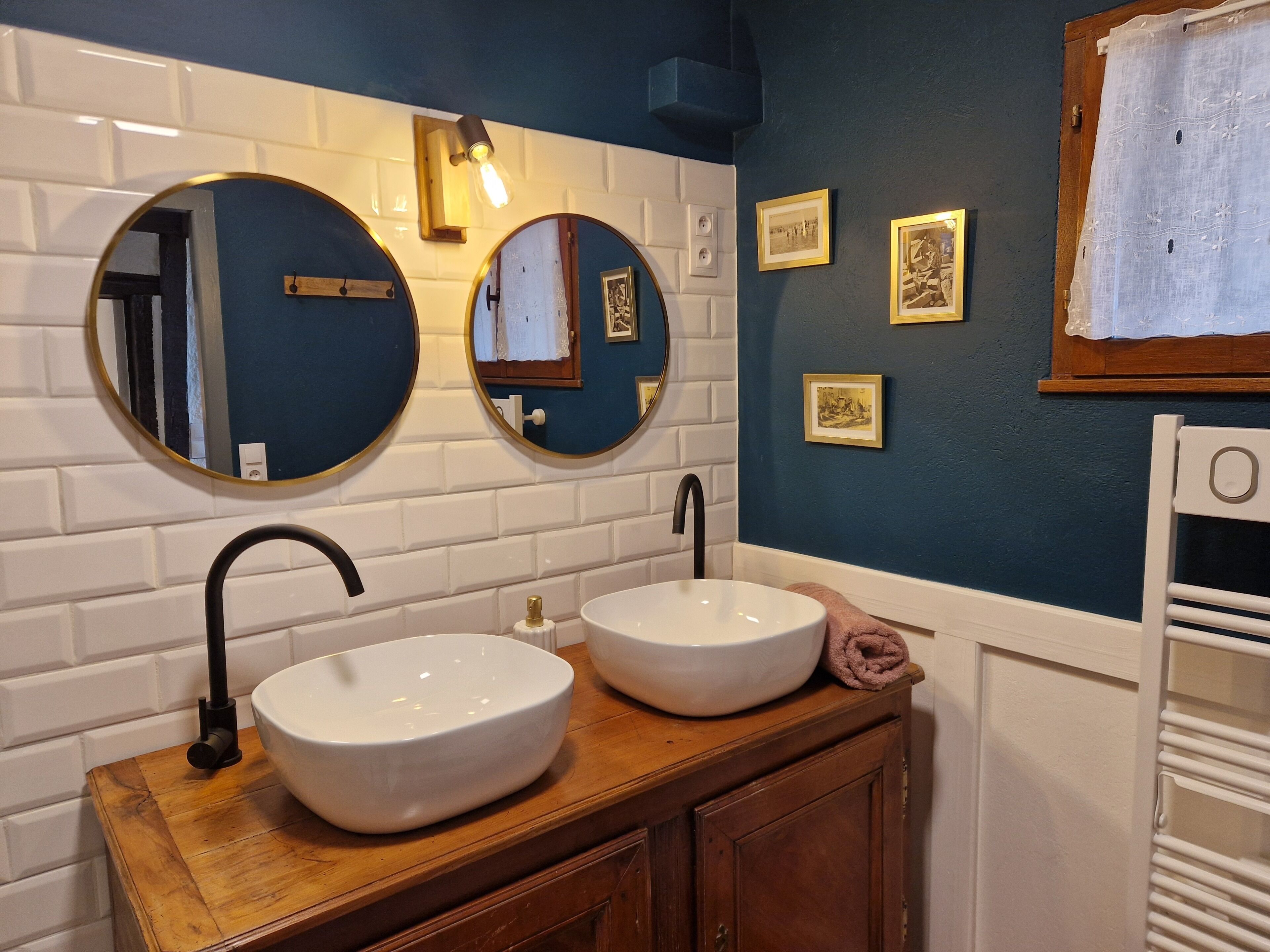 Une salle de bain avec deux miroirs ronds, un lavabo blanc et un meuble-lavabo en bois.