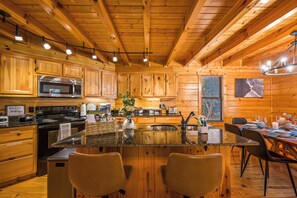 A wooden cabin interior with a kitchen, dining area, and bar seating. - Cozy 2-bedroom cabin in Gatlinburg with hot tub, game loft, pool (Gatlinburg)