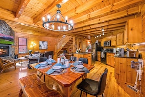 A wooden cabin interior with a dining area, kitchen, fireplace, and a staircase. - Cozy 2-bedroom cabin in Gatlinburg with hot tub, game loft, pool (Gatlinburg)