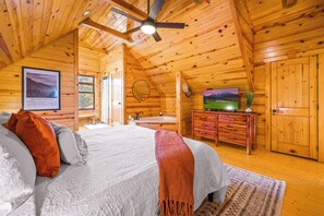 A wooden cabin interior with a bed, a bathroom, and a television. - Cozy 2-bedroom cabin in Gatlinburg with hot tub, game loft, pool (Gatlinburg)