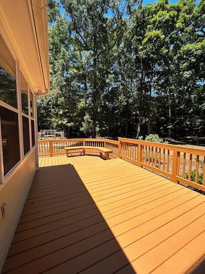 A wooden deck with a railing, a bench, and a view of trees.