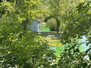 Eine kleine Holzhütte an einem See, umgeben von dichtem Grün.