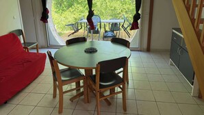Zona pranzo con tavolo rotondo e sedie, divano rosso e vista su una terrazza esterna attraverso un'ampia finestra circolare.