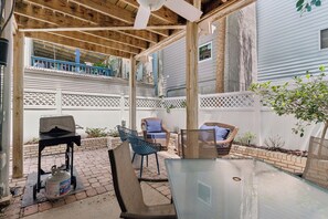 A covered patio with a table and chairs, a grill, and a white fence. - Beach Please sleeps 7 with quick access to the Beach (St Simons Island)