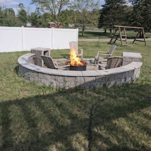 A circular stone fire pit with a fire, surrounded by chairs and a table.