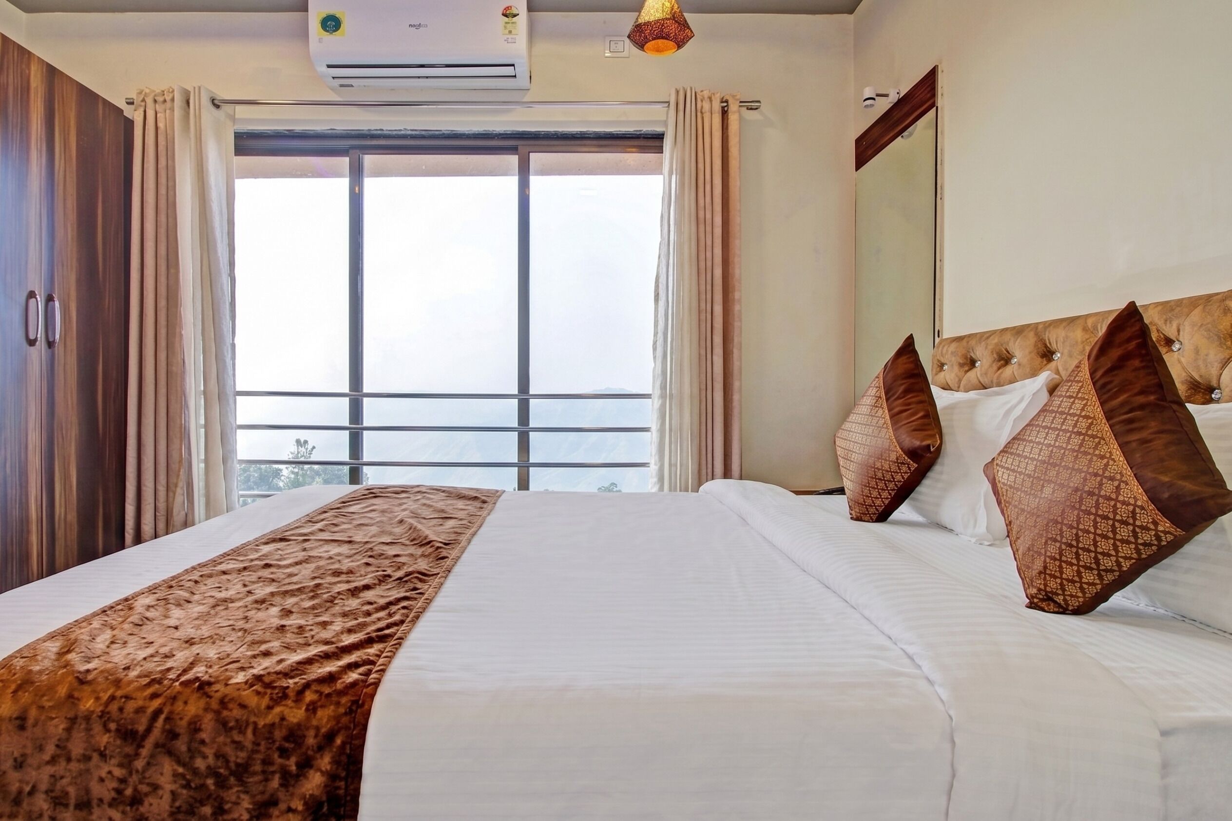 Ein Hotelzimmer mit einem großen Bett, einem Fenster mit Vorhängen, einer Klimaanlage und einem Spiegel an der Wand.