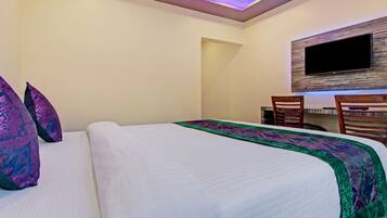 A hotel room with a bed, a desk with chairs, a flat-screen TV mounted on the wall, and a ceiling light.