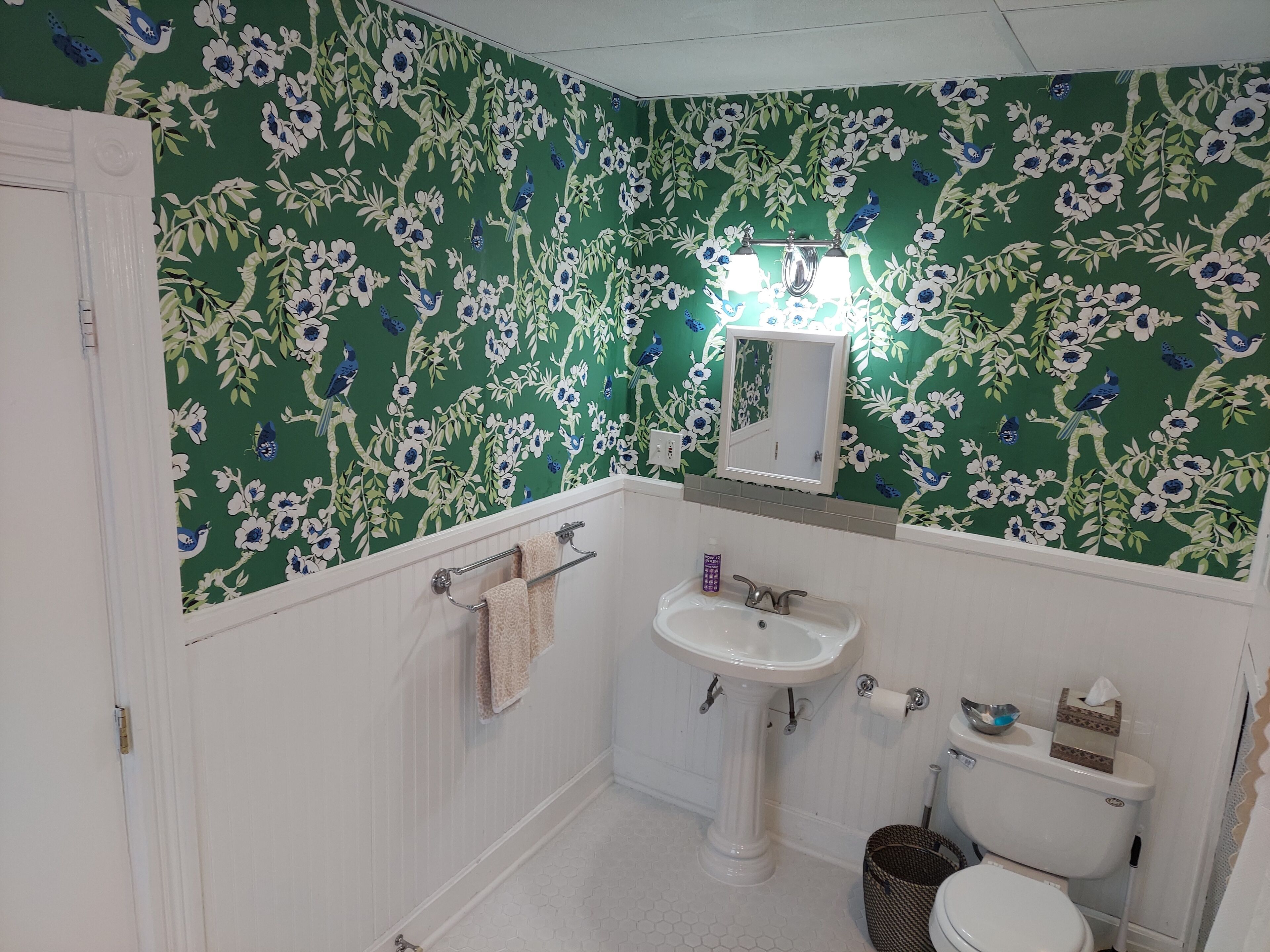 A bathroom with floral wallpaper, a pedestal sink, a toilet, and a mirror above the sink.