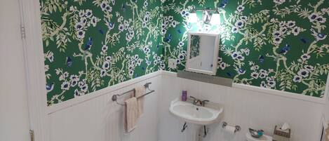 A bathroom with floral wallpaper, a pedestal sink, a toilet, and a mirror above the sink.