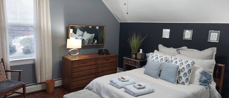 A bedroom with a bed, a nightstand, a dresser, a chair, a ceiling fan, and a window with curtains.