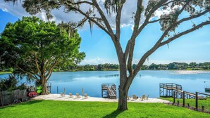 A lakeside property with a dock, chairs, and a tree.