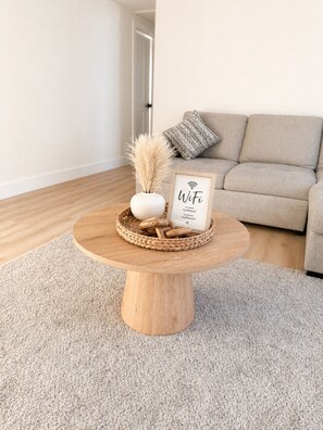 Ein runder Couchtisch aus Holz mit einem gewebten Tablett, einer Vase mit Trockenblumen und einem Rahmen mit der Aufschrift 'WiFi' und Netzwerkinformationen.