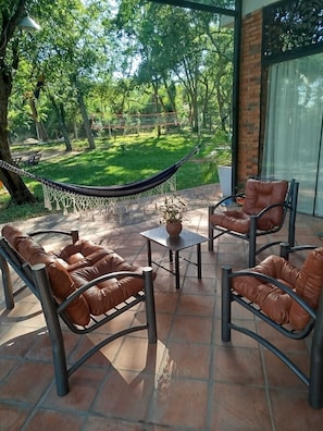 An outdoor patio with a hammock, leather chairs, and a potted plant.