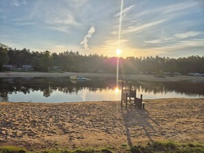 Una playa con una silla y una mesa, un lago tranquilo y un atardecer.