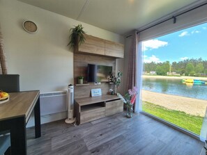 Una habitación moderna con televisión, muebles de madera, una planta y vista a un lago.
