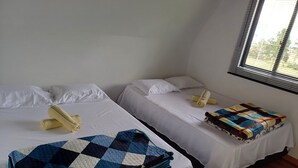 Deux lits simples, avec du linge de lit blanc et une couverture à carreaux bleus sur l’un d’eux.