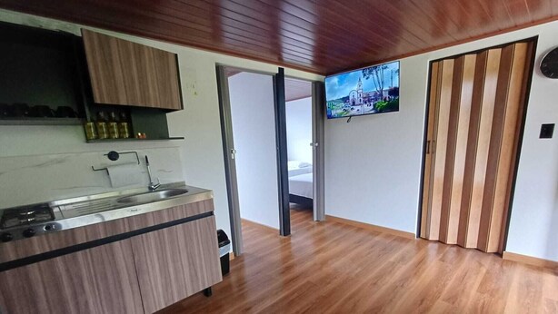 Una cocina moderna con estufa integrada, un lavabo y armarios de madera. Hay un televisor montado en la pared y una puerta corrediza que da a otra habitación.